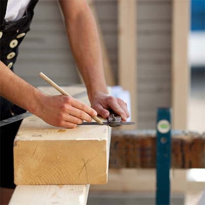 Carpenter marking lumber with a pencil and square, a first step in building cornhole boards