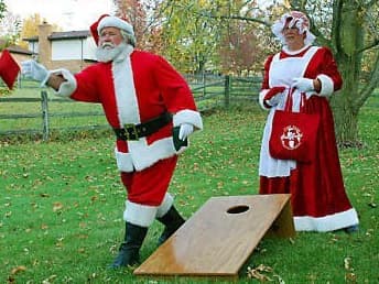 Santa Claus tossing a cornhole bag toward a wooden board while Mrs. Claus watches