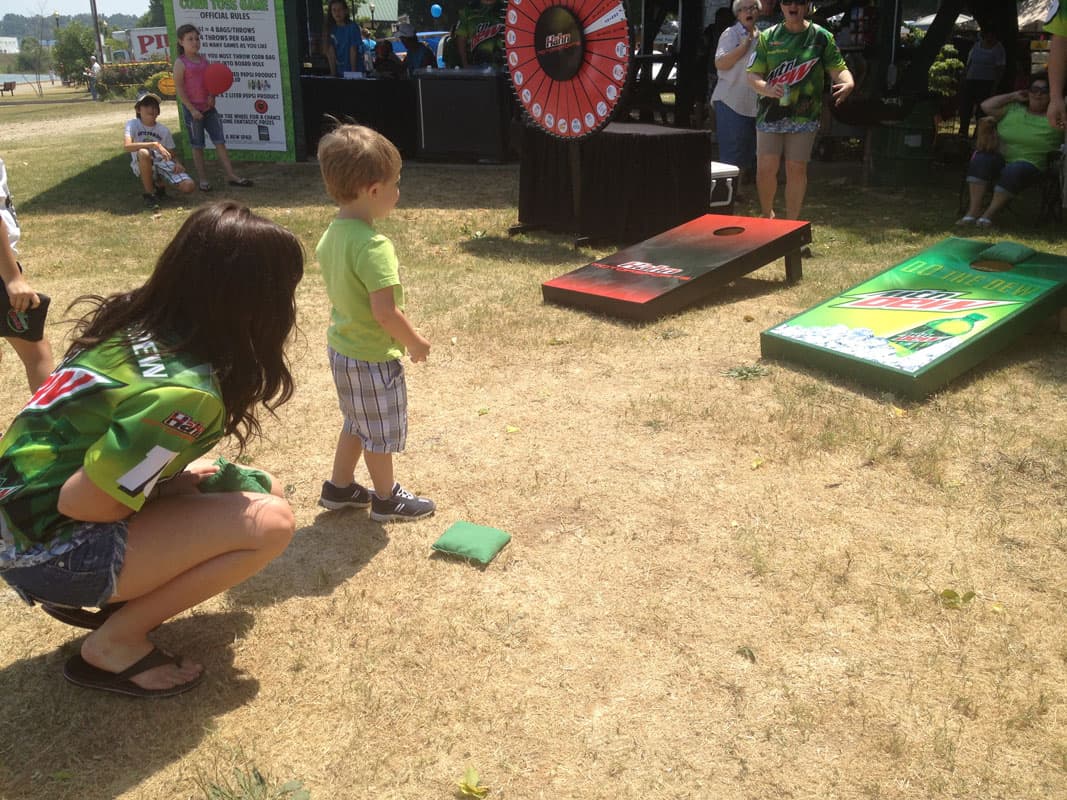 Young boy watching his cornhole bag land short of custom cornhole boards at an outdoor event