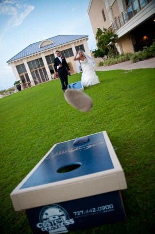 Bride and groom play cornhole at their wedding as a bag flies toward the board