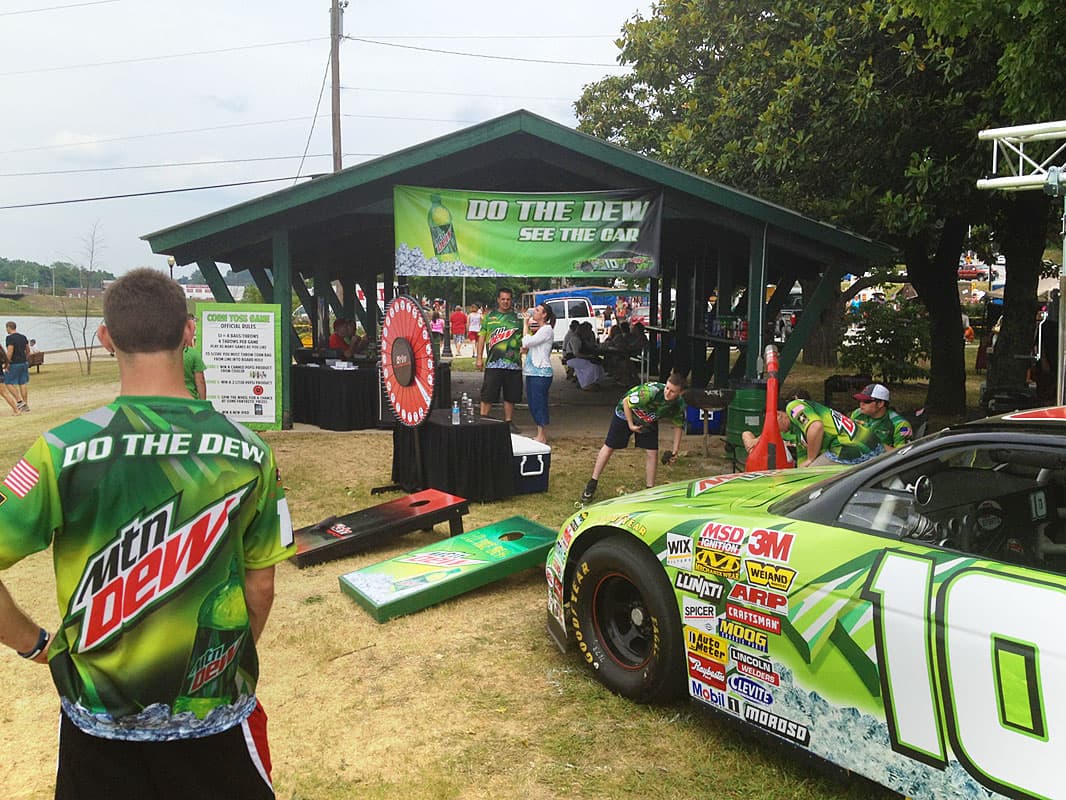 Sponsor-branded custom cornhole boards set up beside a race car at a promotional event