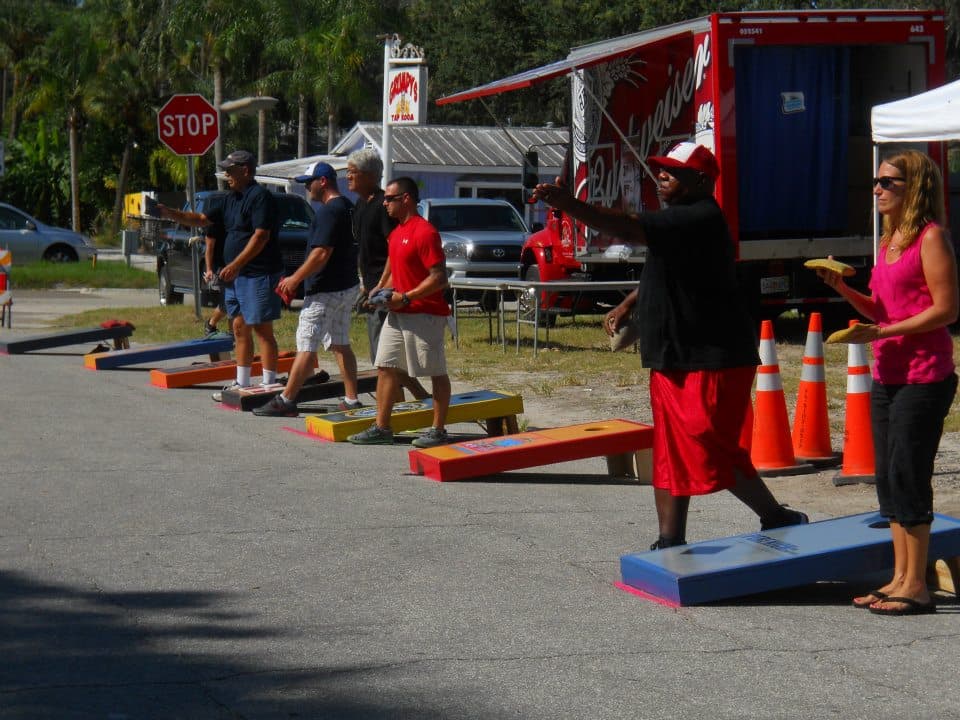 Players tossing bags on a row of custom cornhole boards set up in a parking lot