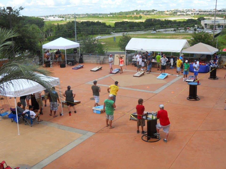 Local cornhole tournament with several courts in play on an outdoor patio under white tents