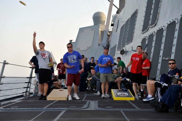 Sailors tossing cornhole bags at custom boards on the deck of a Navy ship