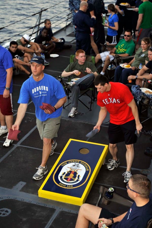 Sailors playing on a custom USS Jason Dunham cornhole board aboard the ship