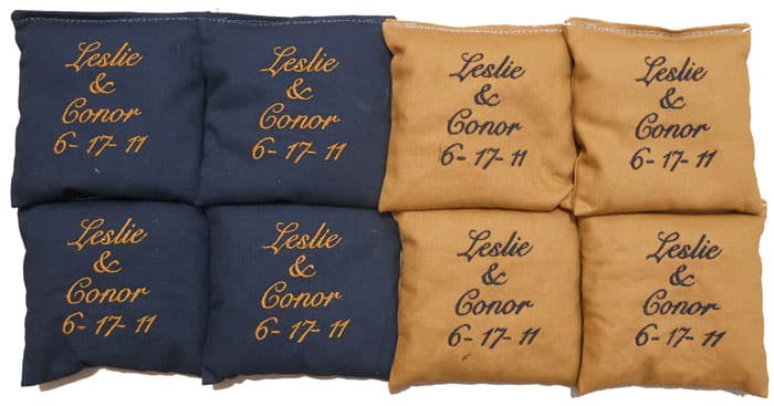 Navy and tan wedding cornhole bags embroidered with the couple’s names and wedding date